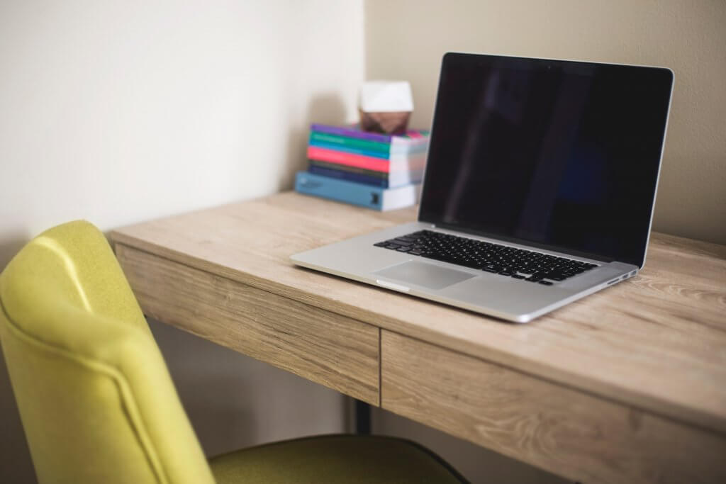 laptop and books on a wooden desk next to a yellow chair